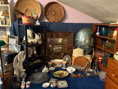 Sale Photo Thumbnail #87: Eclectic assortment of home decor, including woven baskets, decorative porcelain dishes, a black wicker shelf unit, and a painted wooden mirror frame.