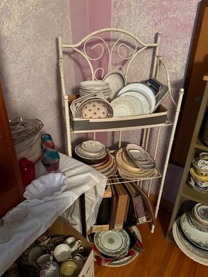 Sale Photo Thumbnail #102: White wrought iron baker's rack holding stacks of vintage china, dishware, and photo albums.