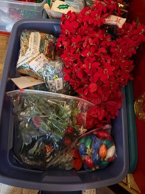 Sale Photo Thumbnail #128: Blue plastic storage bin filled with assorted Christmas decorations, including artificial poinsettias, bagged holly garland, and vintage C9 light bulbs.