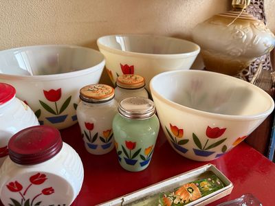 Sale Photo Thumbnail #6: Vintage Fire-King milk glass Tulip pattern mixing bowls, salt and pepper shakers, and grease jars. Mid-20th century collection displaying vibrant red and yellow floral graphics.