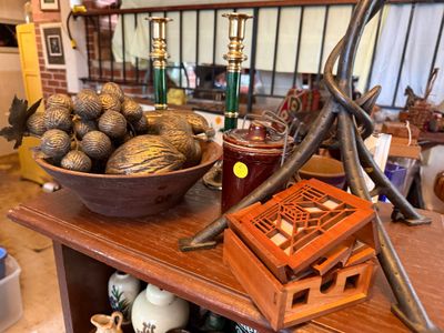 Sale Photo Thumbnail #130: Collection of home decor items including carved wooden decorative fruit in a bowl, a Frank Lloyd Wright style laser-cut wooden coaster set, and brass candle holders.