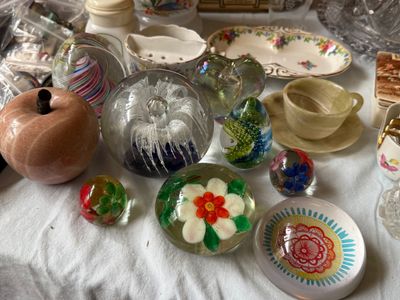 Sale Photo Thumbnail #55: Collection of decorative glass paperweights, a pink alabaster marble apple, and an onyx cup and saucer set displayed alongside vintage ceramic dishes.