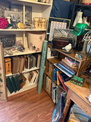 Sale Photo Thumbnail #83: Densely packed corner shelves with vintage books, framed photographs, decorative ceramics, a green banker's lamp, and various home decor items.