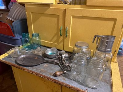Sale Photo Thumbnail #116: Assortment of vintage kitchenware including Ball mason jars, a cast iron griddle, hand-crank meat grinder, flour sifter, and glass citrus juicers.