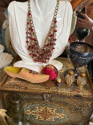 Sale Photo Thumbnail #21: Collection of vintage decorative items including a red beaded multi-strand necklace on a bust display, a painted miniature wooden shoe, a small red coin purse, and a pair of glass salt and pepper shakers atop a patterned tin box.