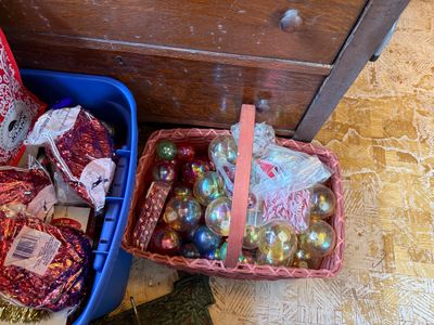 Sale Photo Thumbnail #135: Pink woven storage basket filled with vintage glass Christmas baubles, tinsel, and holiday decorations next to a blue plastic tote.
