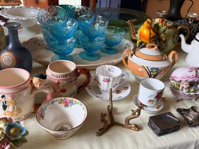 Sale Photo Thumbnail #48: Collection of vintage porcelain and glassware, including blue textured sherbet dishes, floral teacups, decorative character mugs, and small brass trinkets.