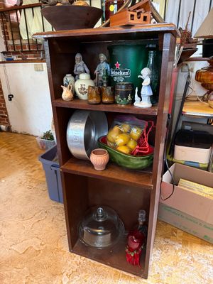 Sale Photo Thumbnail #131: Rustic dark wood three-tier bookshelf display filled with various collectibles including porcelain figurines, a Heineken bucket, vintage kitchenware, and a glass cake dome.