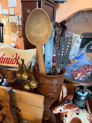 Sale Photo Thumbnail #145: Vintage carved wooden spoon displayed in a brown stoneware crock alongside kitchen utensils and decorative trinkets.