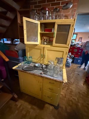 Sale Photo Thumbnail #112: Vintage painted yellow Sellers-style Hoosier cabinet, featuring mesh-paneled upper doors and a metal work surface lined with assorted antique glassware and kitchenware.