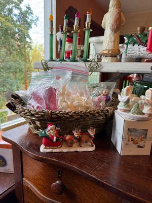 Sale Photo Thumbnail #132: Collection of holiday decorations, including a woven basket with plastic bags of small ornaments, a Santa in a sleigh figurine, and vintage candle lights on a shelf.