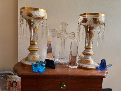 Sale Photo Thumbnail #82: Collection of glass and crystal decorative items, featuring a pair of hand-painted porcelain or milk glass luster lamps with gold leaf detail and crystal prisms, alongside crystal paperweights and small glass bird figurines.
