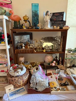 Sale Photo Thumbnail #69: Collection of eclectic home decor and collectibles arranged on a wooden shelving unit, including an angel figurine, flamingo statuette, glassware, framed artwork, and trinket boxes.