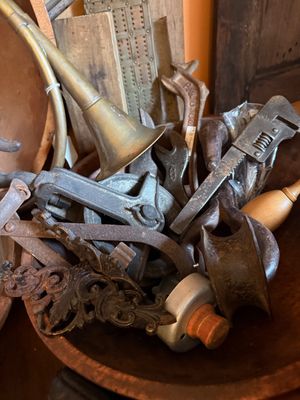 Sale Photo Thumbnail #144: Collection of vintage tools, hardware, and decorative metal pieces, including a brass horn, monkey wrench, cast iron brackets, and pulleys displayed in a wooden bowl.