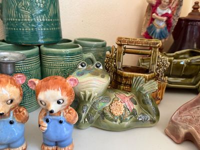 Sale Photo Thumbnail #34: Collection of vintage ceramic figurines, including a pair of bear-shaped salt and pepper shakers in blue overalls, a reclining frog planter, and green glazed steins.