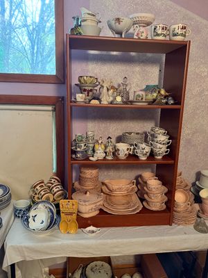 Sale Photo Thumbnail #98: Collection of vintage porcelain and glassware display, featuring pink depression glass dish sets, teacups, saucers, and decorative figurines on a wood bookcase.