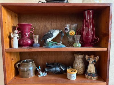Sale Photo Thumbnail #7: Collection of decorative collectibles displayed on a wooden shelf, including roseville-style pottery vases, hand-painted glass, bird and angel figurines, and stoneware jars.