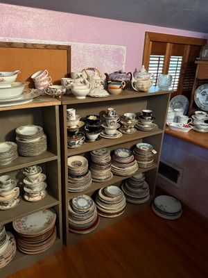 Sale Photo Thumbnail #103: Large collection of vintage porcelain and china tableware, including teacups, saucers, teapots, and stacked dinner plates displayed on wooden shelving units.