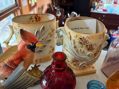 Sale Photo Thumbnail #62: Collection of vintage decorative ceramics and glassware, including a Red Wing pottery #1107 floral vase, a cardinal-figured planter, and a red optic pattern glass bottle.