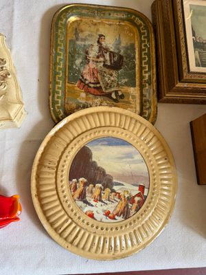 Sale Photo Thumbnail #15: Pair of vintage decorated tin trays, including a rectangular tray featuring a woman playing an accordion and a round tray with a embossed pale yellow border around a rural winter scene.
