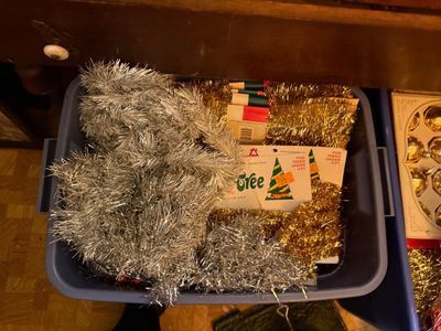 Sale Photo Thumbnail #138: Plastic storage tote filled with vintage silver and gold tinsel garland, including packaged holiday tree decorations.