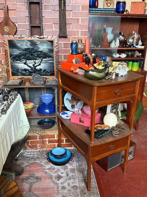 Sale Photo Thumbnail #66: Mid-century wooden side table set stacked with various collectibles, ceramics, glass decor, and framed artwork displayed in a home setting.