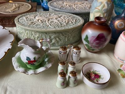 Sale Photo Thumbnail #49: Collection of vintage decorative tableware and trinket boxes, featuring miniature salt and pepper shakers, a small holly-patterned creamer on a saucer, floral-printed art glass vase, and carved celadon-style trinket boxes with peacock reliefs.