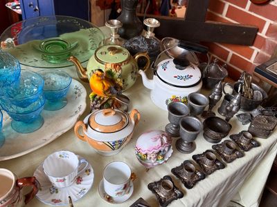 Sale Photo Thumbnail #44: Assorted vintage tabletop items, featuring blue glass cups, green uranium style glass, ceramic teapots, pewter goblets, and silver-tone metal candle holders.