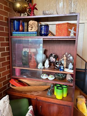 Sale Photo Thumbnail #65: Mid-century wooden hutch displaying various collectibles, glassware, figurines, books, and home decor items.