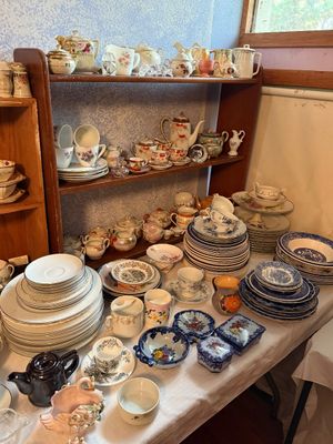 Sale Photo Thumbnail #99: Collection of vintage porcelain dinnerware, teacups, saucers, and decorative teapots displayed on a table and wooden shelving unit.