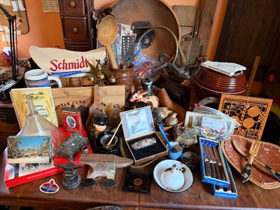 Sale Photo Thumbnail #141: Tabletop collection of vintage primitives, collectibles, and kitchenware, including a small cast-iron anvil, Schmidt beer canvas bag, wooden utensils, and boxed cutlery.