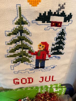 Sale Photo Thumbnail #117: Scandinavian cross-stitch wall hanging featuring a Tomte figure, pine trees, and a cottage with 'God Jul' lettering.