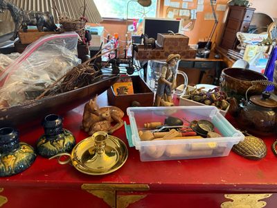 Sale Photo Thumbnail #126: An eclectic mix of vintage decor items displayed on a red cabinet, including brass chambersticks, carved wooden deer figurines, pottery, and a clear plastic bin filled with small collectibles.