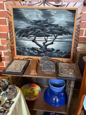 Sale Photo Thumbnail #45: Framed black velvet landscape painting of a coastal cypress tree, displayed alongside religious icon plaques, bookends, and colorful ceramic bowls.