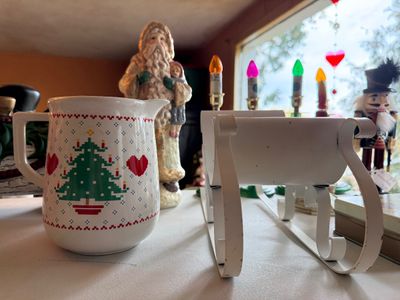 Sale Photo Thumbnail #118: Collection of Christmas decor including a ceramic pitcher with pixelated tree motif, white metal sleigh, Santa figurine, and a nutcracker.