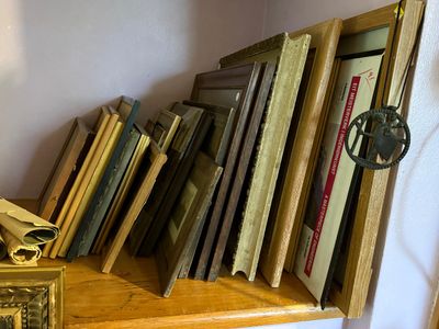 Sale Photo Thumbnail #92: Collection of vintage picture frames leaning against a wall on a wooden shelf.