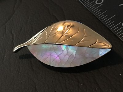 Sale Photo Thumbnail #70: A vintage Liz Claiborne leaf brooch featuring a gold-tone metal half with detailed veining and a iridescent mother-of-pearl (or shell inlay) half. Signed 'LC' on the back. Measures approximately 2.25 inches long. Features a standard rollover safety clasp 
