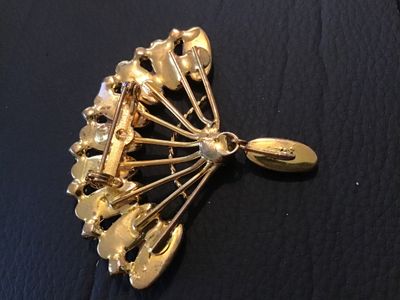 Sale Photo Thumbnail #80: A vintage fan-shaped costume jewelry brooch featuring gold-tone metal, brown marquise/cabochon stones with a cat's eye sheen, clear rhinestone accents along the outer rim, and a dangling accent piece. Measures approximately 2.5 inches across. Shows minor 