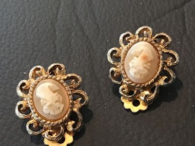 Sale Photo Thumbnail #85: Pair of vintage clip-on earrings featuring Shell cameo portrait  set within ornate, filigree-style gold-tone metal frames. The clips show some age-related patina and finish wear on the reverse side. Overall good vintage condition.