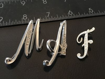 Sale Photo Thumbnail #111: Set of three silver-tone initial letter brooches featuring the letters 'M', 'A', and 'F'. Each brooch is set with clear rhinestones in a script design with pin-back closures. Brooches measure approximately 1.25 to 2.25 inches in height. Items show light w