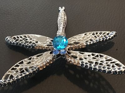 Sale Photo Thumbnail #93: Silver-tone dragonfly brooch featuring intricate openwork filigree wings, dark blue and clear accent rhinestones, and a large bright blue center stone. Includes a standard pin back with a safety clasp. Measures approximately 2.5 inches long. In good condi