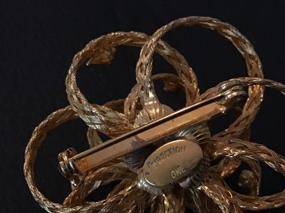 Sale Photo Thumbnail #23: Vintage gold-tone floral brooch featuring braided wire loops accents and set with clear rhinestones. Marked 'DIRECTION ONE' on an oval plaque on the back. Features a standard pin stem and roll-over safety clasp. In good vintage condition with light finish