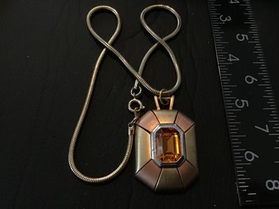 Sale Photo Thumbnail #69: Vintage Napier costume jewelry necklace featuring an emerald-cut amber/citrine color glass or rhinestone centerpiece set in a silver-tone bezel. The geometric pendant features alternating gold-tone and rose gold-tone panels with a textured back stamped wi