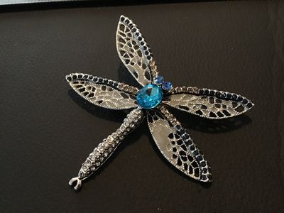 Sale Photo Thumbnail #92: Silver-tone dragonfly brooch featuring intricate openwork filigree wings, dark blue and clear accent rhinestones, and a large bright blue center stone. Includes a standard pin back with a safety clasp. Measures approximately 2.5 inches long. In good condi