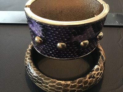 Sale Photo Thumbnail #97: Lot of two fashion bracelets featuring snakeskin texturing. Includes one wide gold-tone hinged cuff bracelet with purple snakeskin-style inlay and gold-tone stud accents, and one rounded slip-on bangle bracelet with neutral gray and brown snakeskin patter