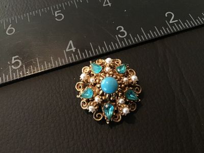Sale Photo Thumbnail #4: A vintage ornate gold-tone brooch/pin by Florenza featuring a central faux turquoise cabochon surrounded by faux pearls and teardrop light blue rhinestones. Filigree/scrollwork detailing on a textured gold-tone setting. Signed FLORENZA© on the back. Meas