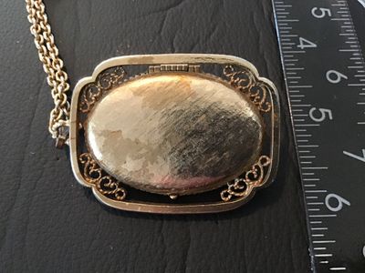 Sale Photo Thumbnail #9: Vintage Avon gold tone filigree locket necklace featuring a blue faux lapis lazuli cabochon stone on the front cover. The locket opens on a side hinge to reveal space inside, marked AVON ©. Pendant measures approximately 2 inches in length. Comes attache