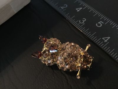 Sale Photo Thumbnail #29: Gold tone owl-shaped brooch featuring paved brown and champagne-colored rhinestones with dark amber glass accents for the ears and beak. Measures approximately 1.5 inches in length. Features a rollover safety clasp on the back. Good pre-owned condition wi