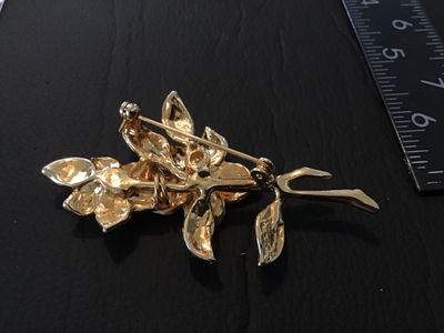 Sale Photo Thumbnail #43: A gold-tone brooch featuring purple enamel flower blooms, green enamel leaves, and clear rhinestone accents. Measures approximately 2.5 inches long. Features a standard pin back with standard clasp. In good condition with light wear.