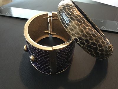 Sale Photo Thumbnail #96: Lot of two fashion bracelets featuring snakeskin texturing. Includes one wide gold-tone hinged cuff bracelet with purple snakeskin-style inlay and gold-tone stud accents, and one rounded slip-on bangle bracelet with neutral gray and brown snakeskin patter